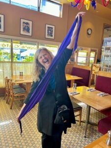 SARK smiles big while holding a stretched out purple scarf